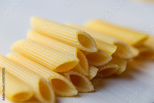 Pasta; raw Penne Rigate, on a white wooden surface.