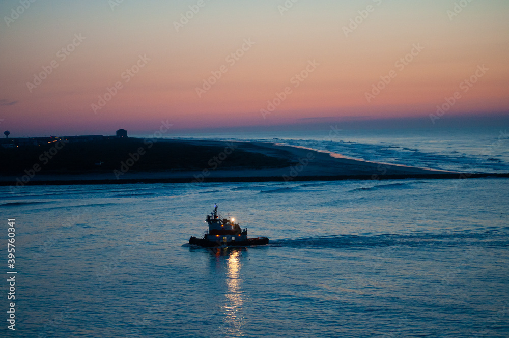 A fishing boat returns to the safety of Absecon Inlet in Atlantic City NJ after visiting the fishing ground in the Atlantic Ocean. Fishing boat launches after sunset to end it's the day!