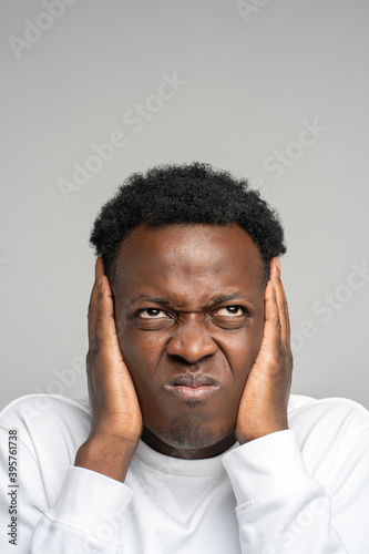 фотографія Closeup angry mad stressed afro man covering his ears and looking up, hears annoying loud noise from upstairs neighbors isolated on studio grey background