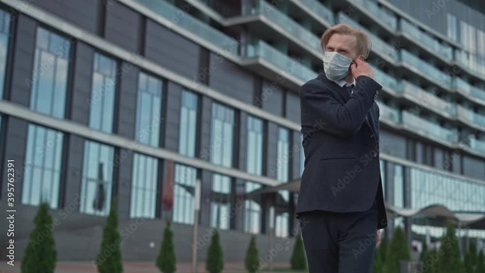 Handsome millennial businessman start-up developer office executive manager removes, rips off his mask and enjoy the fresh air near mirrored city center. Portrait. Quarantine. Workspace and pandemic.