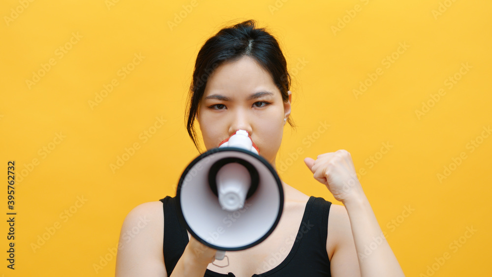 Young female college student talking at the camera with a megaphone in the studio. Isolated on yellow background. High quality photo Young female college student talking at the camera with a megaphone in the studio. Isolated on yellow background. High quality photo