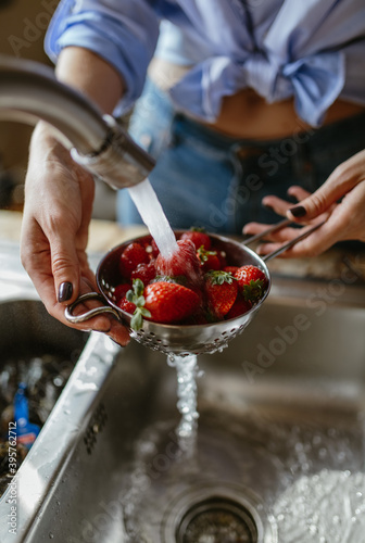 Girl washing fresh strawberries, beautiful kitchen