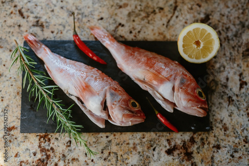Fish with lemon, rosemary and red pepper on a cooking board, scorpaena