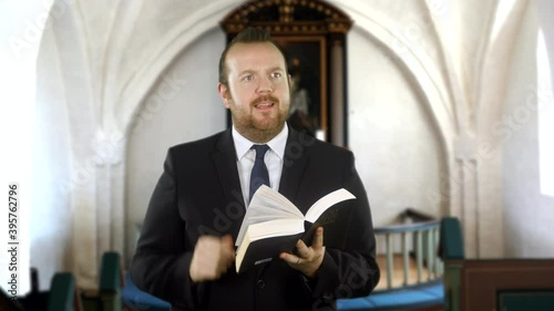 A preacher reads from the Holy Bible in church. The pastor makes a speech in front to the congregation. The minister is bearing a black suit and tie. photo