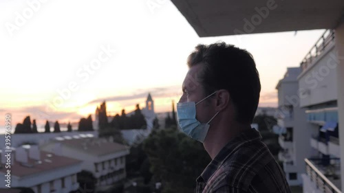 man hotel guest wearing protective mask to protect from coronavirus, male on balcony with sea view