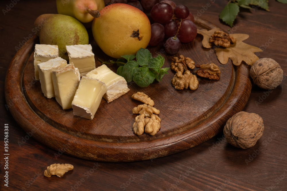 Cheese plate with fruits, grapes, nuts on a dark wooden plate and wooden table. Wine snacks set: selection of cheese, grapes, pear and walnuts on a wooden board. Cheese plate with fruits, grapes, nuts on a dark wooden plate and wooden table. Wine snacks set: selection of cheese, grapes, pear and walnuts on a wooden board.