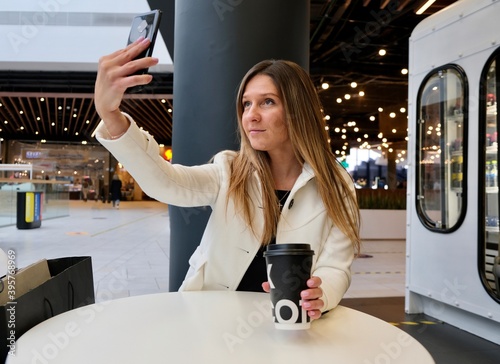 A young woman takes a selfie in a cafe. Using a smartphone. Girl taking selfie with mobile phone