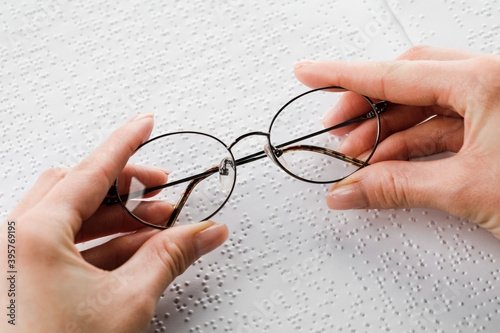 A woman holds black-rimmed glasses against the background of an open textbook reading books in Braille