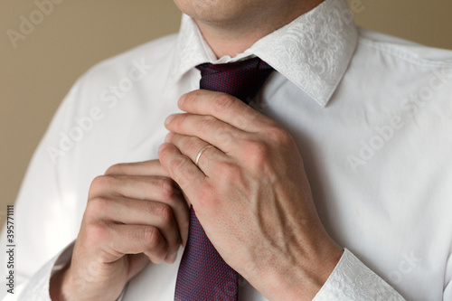 A married man with a ring on his hand straightens his tie.