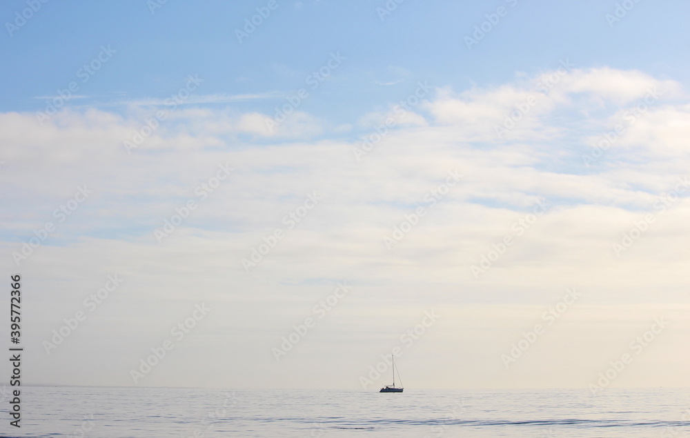 A photograph of a yacht on the horizon with big sky and ocean. Calm, mindfulness concept