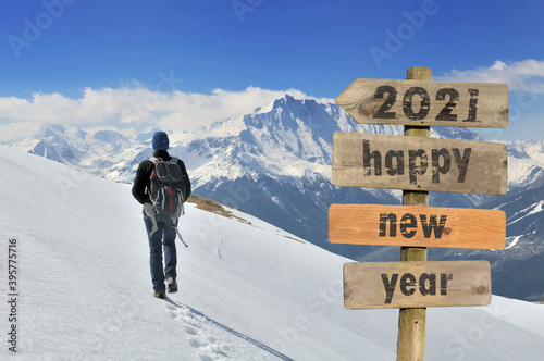 2021 happy new year wrtten on a postsign with a hiker walking on the snow in a mountain background photo
