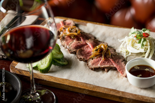 slices of roast beef appetizer with balsamic sauce and glass of red wine on wooden board