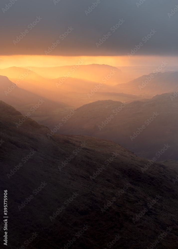 Majestic golden rays of sunlight breaking through clouds, illuminating the Eskdale Valley in the Lake District, UK.