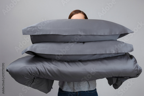 The woman is holding a warm duvet and gray feather pillows. Bedding for sleeping.