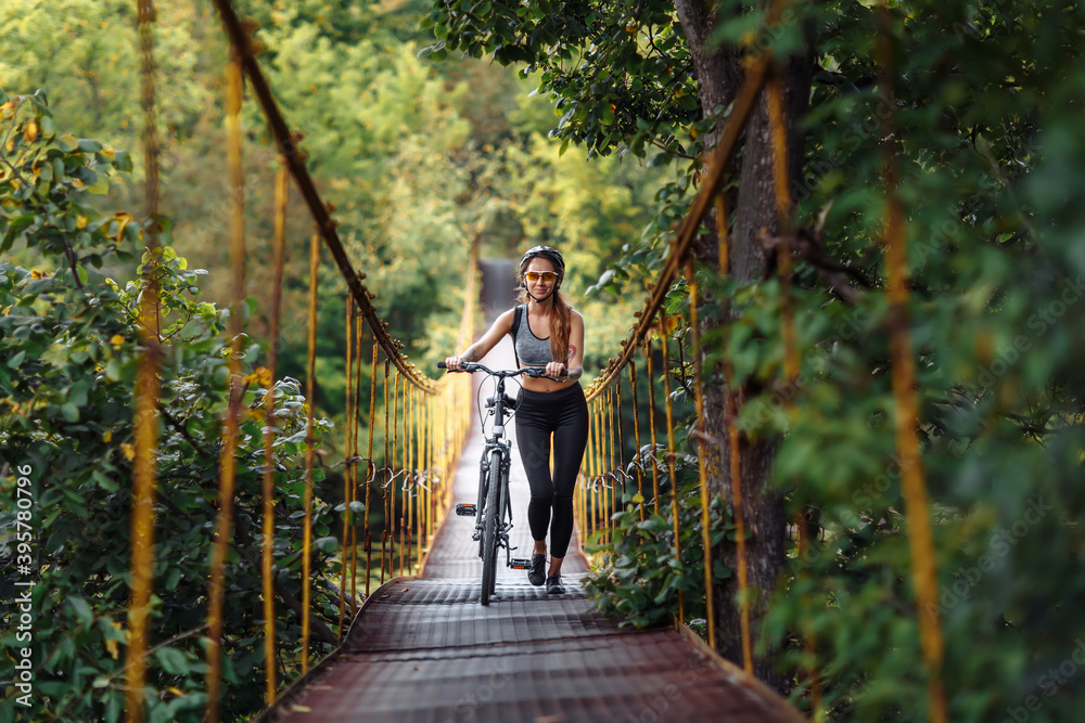 Fit young woman wearing sportswear with her bicycle on suspension bridge at autumn