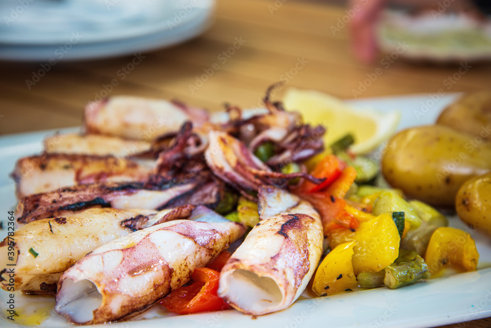 Delicious grilled whole squid with tomatoes, cucumber slices, Beetroots pieces and green dandelions served in white plate for a healthy Mediterranean meal