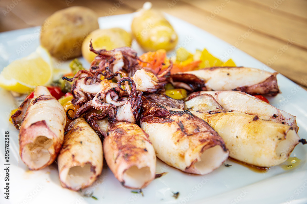 Delicious grilled whole squid with tomatoes, cucumber slices, Beetroots pieces and green dandelions served in white plate for a healthy Mediterranean meal