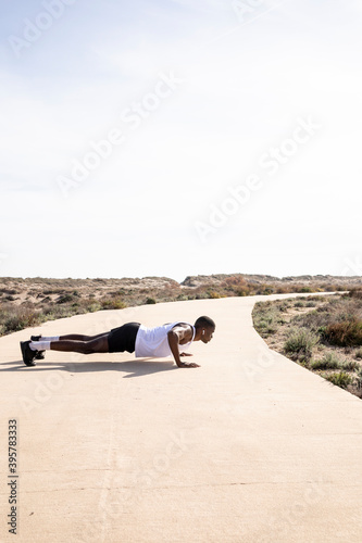 Vertical shot of young black runner in profile doing push-ups and facing forward.