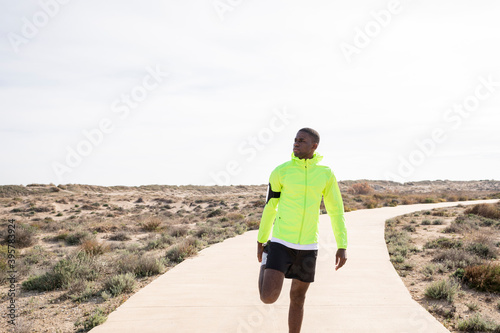 Young black runner in a yellow rain jacket stretching his legs before or after training. © menudencias