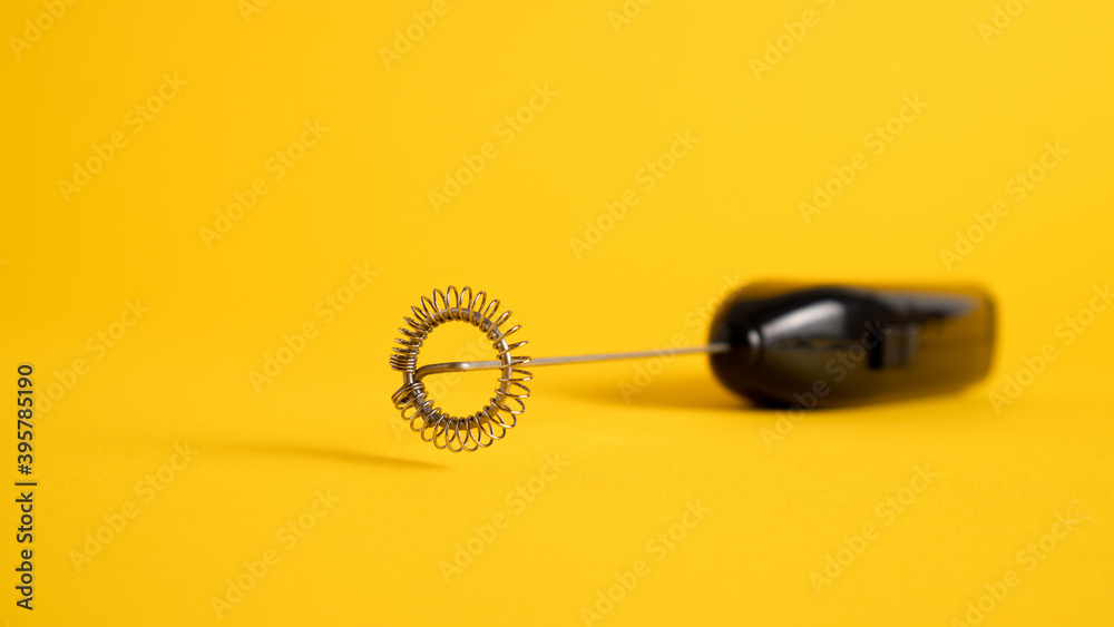 Black handheld milk steamer on yellow background. Handheld frother. Hand whisk. Foam maker. Mini milk mixer Black handheld milk steamer on yellow background. Handheld frother. Hand whisk. Foam maker. Mini milk mixer