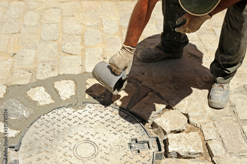 Bricklayer pouring liquid cement on the sores of the paving stone. Paving a street in the traditional way with cobblestones in Seville, Spain photo
