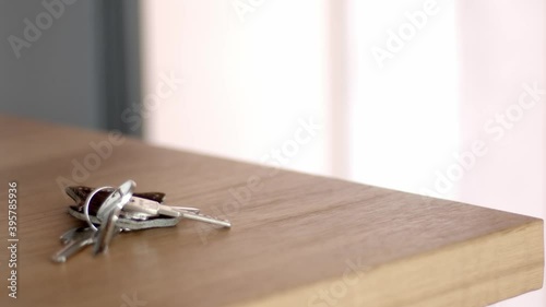 A hand in a beige jacket opens the door on the background, throws the keys from the apartment on the wooden table and closes the door from the inside. 4k close up video, still high quality footage.