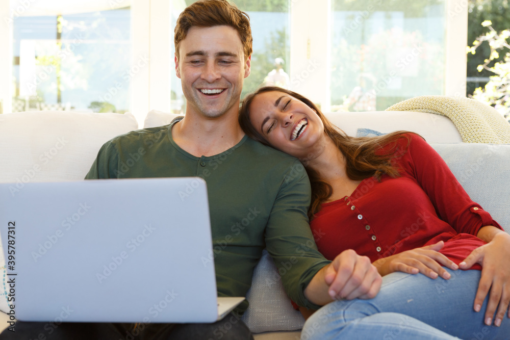Caucasian couple sitting on a couch using laptop Caucasian couple sitting on a couch using laptop