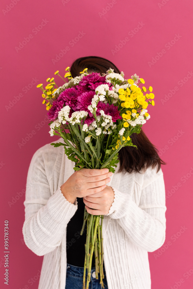 Caucasian woman covering her face with bouquet of flowers on pink Caucasian woman covering her face with bouquet of flowers on pink
