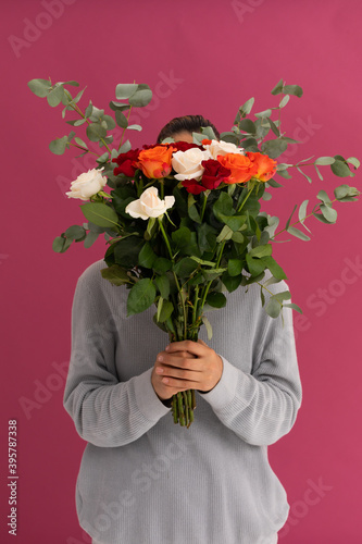 Caucasian woman covering her face with bouquet of roses on pink