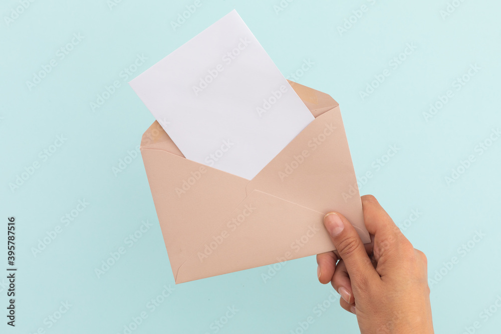 Hand of caucasian woman holding opened envelope with letter over pale blue background