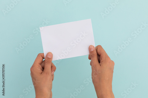 Two hands of caucasian woman holding white paper over pale blue background