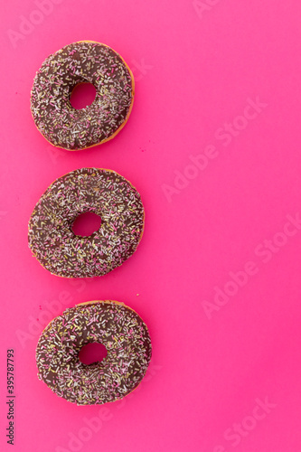 High angle view of three chocolate donuts with sprinkles on pink background