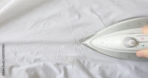 Man hand irons white clothes with a steam iron on an Ironing board. Top view. 