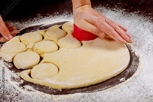 Woman cuts out dough with round mold for making buns, dounuts. photo