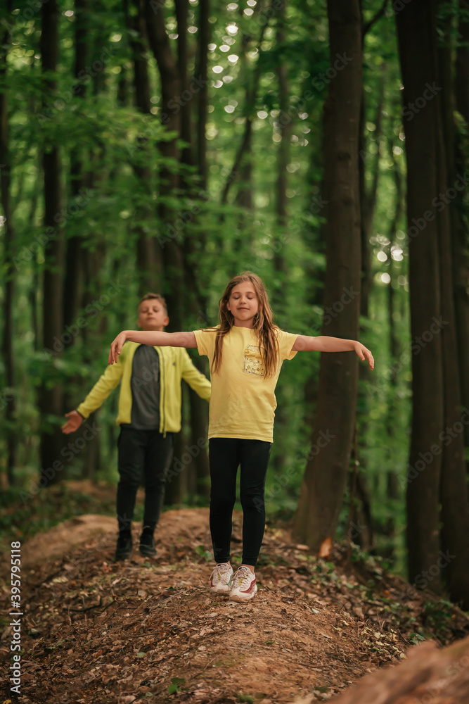  Little boy and girl with raised arms enjoying the fresh air in beautiful forest.