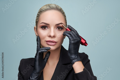 Permanent makeup artist woman. She holds a tattoo machine in her hands. Fashion, beauty, makeup, cosmetics, health, spa, wellness.