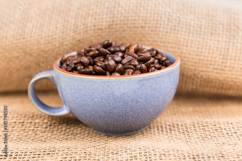 Cup filled with brown roasted coffee beans over folded burlap background