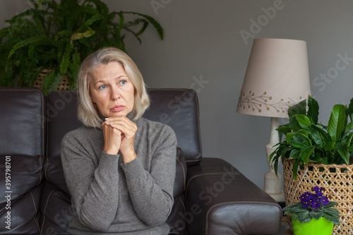 А woman at the age is sitting alone on the couch. Sadness, loneliness.