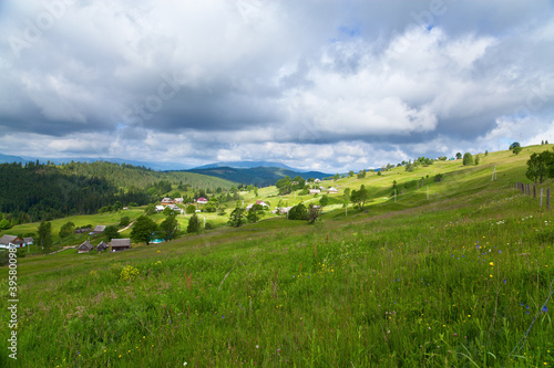 Rural mountain landscape, village and geen meadows, mountains on the horizon, dark sky above.