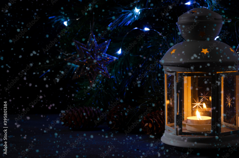 White candle lantern with burning candle. Blurred spruce brunch and garland lights on the dark background. Falling snow. Retro style picture. White candle lantern with burning candle. Blurred spruce brunch and garland lights on the dark background. Falling snow. Retro style picture.