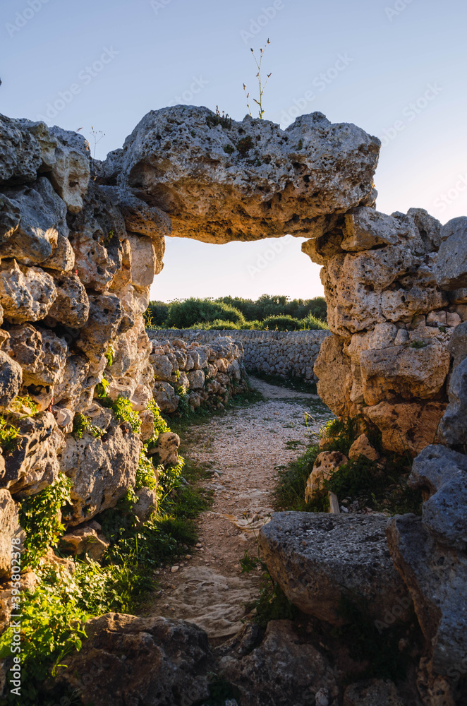 Landscape photograph of an arch made with stones in ancient Menorca giving way to a path between stone walls.