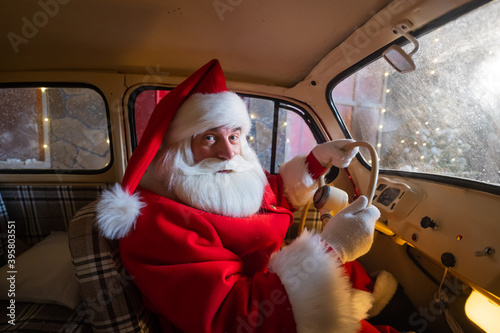 Portrait of santa claus driving a car loaded with a Christmas tree and gifts photo