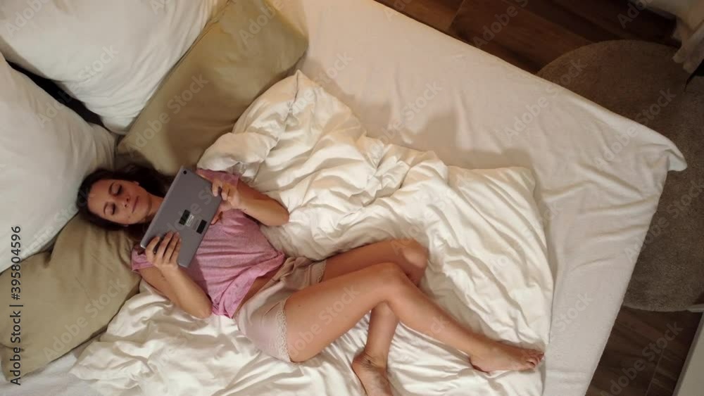 Young sexy woman lies relaxed on her bed with her tablet computer - videoclip Young sexy woman lies relaxed on her bed with her tablet computer - videoclip