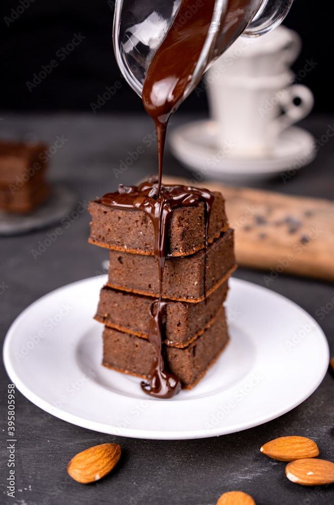Cocoa brownies pouring with melted dark chocolate on a white plate. Black background Cocoa brownies pouring with melted dark chocolate on a white plate. Black background