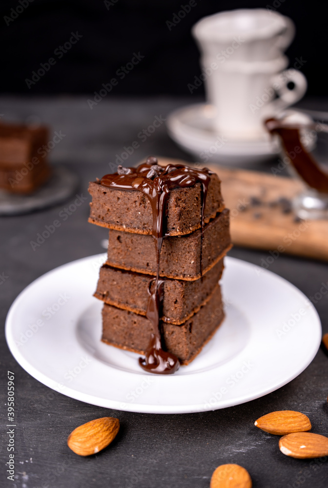 Cocoa brownies pouring with melted dark chocolate on a white plate. Black background Cocoa brownies pouring with melted dark chocolate on a white plate. Black background