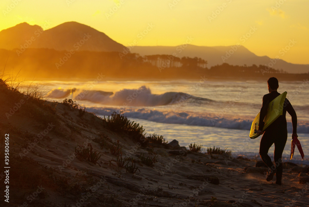 Man walking into the water on a beach with waves and perfect sunset Man walking into the water on a beach with waves and perfect sunset