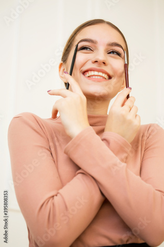 Portrait of a beautiful cute young girl standing with two eyebrow makeup brushes in her hands.The girl applies a brush to her eyebrows