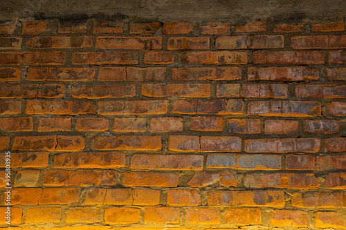 Background of old vintage red brick wall with concrete, illuminated from below with yellow light, dried up bricks texture, Grunge background