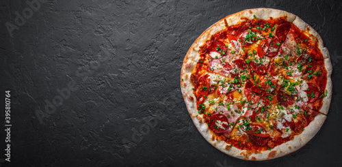 Pizza with Mozzarella cheese, ham, tomato sauce, pepper, salami. Italian pizza on Dark grey black slate background