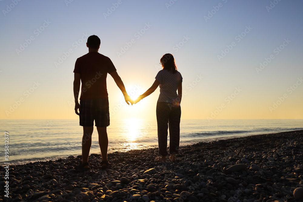 Loving couple hold hands in the rays of the setting sun on the seashore. Concept of love and happiness together